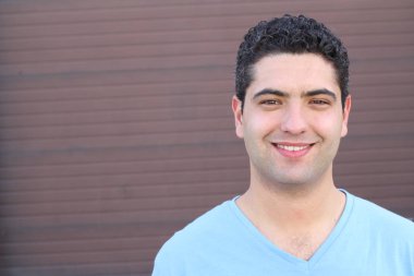 close-up portrait of handsome young man in blue t-shirt in front of brown wall