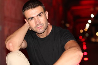 Geceleri sokakta siyah tişörtlü yakışıklı bir adamın yakın plan portresi.