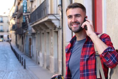 Sırt çantalı yakışıklı genç adamın eski şehir caddesinde telefonla konuşurken yakın plan portresi.