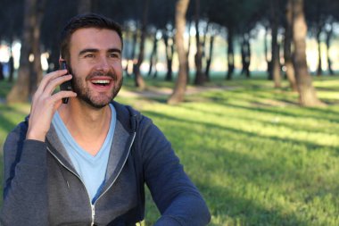 Yeşil Park 'ta telefonla konuşan sıradan giyinmiş yakışıklı genç adamın yakın plan portresi.