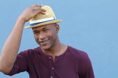 Mavi duvarın önünde şapkalı yakışıklı Afro-Amerikan bir adamın yakın plan portresi.