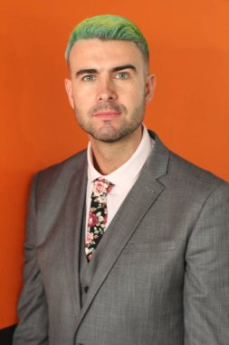 Turuncu arka planda duran yeşil saçlı zarif yakışıklı adam.