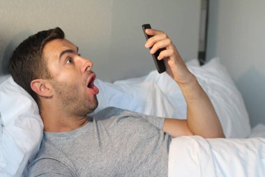Evdeki yatakta akıllı telefon kullanan yakışıklı bir gencin yakın plan portresi.