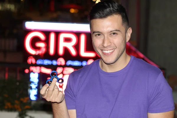 close-up portrait of handsome young man with fidget spinner in front of neon girls lettering on street