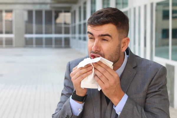 close-up portrait of handsome young businessman sneezing in napkin on street
