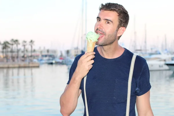 日没のヨットの前で港でアイスクリームを食べるスタイリッシュな服のハンサムな若い男のクローズアップ肖像画 — ストック写真