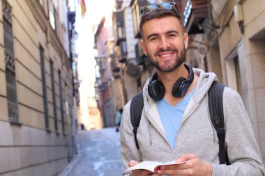 Sırt çantalı ve kitaplı yakışıklı genç adamın şehir sokaklarındaki yakın plan portresi.