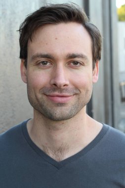 Gri duvarın önünde sıradan giyinmiş yakışıklı bir gencin yakın plan portresi.