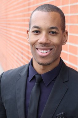 Tuğla duvarın önünde siyah takım elbiseli yakışıklı Afro-Amerikan iş adamının yakın plan portresi.