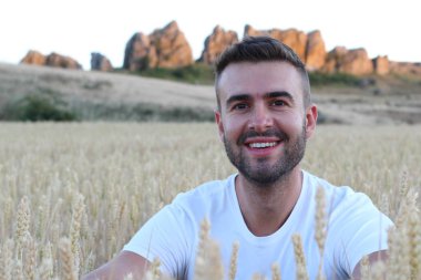 Genç adam buğday tarlasında dururken gülümsüyor. 