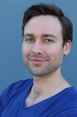 Mavi duvarın önünde sıradan giyinmiş yakışıklı bir gencin yakın plan portresi.