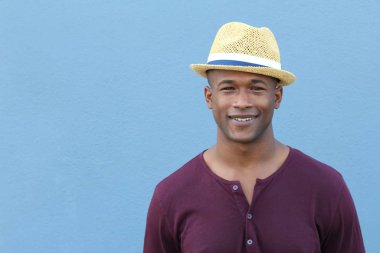 Mavi duvarın önünde şapkalı yakışıklı Afro-Amerikan bir adamın yakın plan portresi.