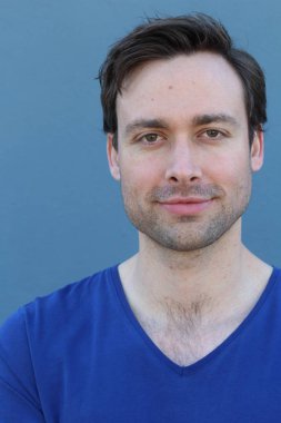 Mavi duvarın önünde sıradan giyinmiş yakışıklı bir gencin yakın plan portresi.