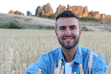 Genç adam buğday tarlasında dururken gülümsüyor. 