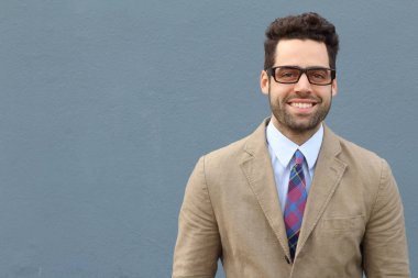 Gri duvarın önünde bej takım elbiseli yakışıklı genç işadamının yakın plan portresi.