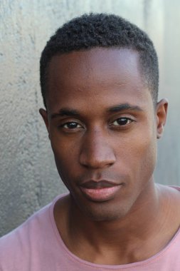 Gri duvarın önünde pembe tişörtlü yakışıklı genç adamın yakın plan portresi.