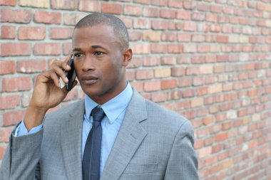 Gri takım elbiseli, duvarın önünde telefonla konuşan üzgün genç işadamının yakın plan portresi.