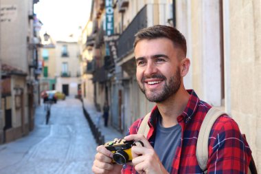 Eski şehir caddesinde sırt çantalı ve klasik kameralı yakışıklı bir gencin yakın plan portresi.