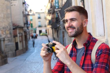 Eski şehir caddesinde sırt çantalı ve klasik kameralı yakışıklı bir gencin yakın plan portresi.