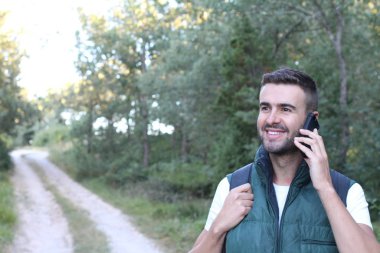 Doğada telefonla konuşan yakışıklı genç adamın yakın plan portresi.