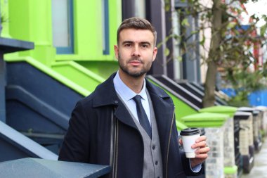 Yakışıklı genç iş adamının yakın plan portresi. Sıcak palto ve sokakta bir fincan kağıt kahve.