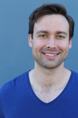 Mavi duvarın önünde sıradan giyinmiş yakışıklı bir gencin yakın plan portresi.