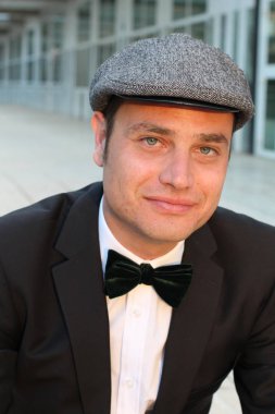 Siyah takım elbiseli, papyonlu ve şapkalı yakışıklı bir adamın yakın plan portresi.