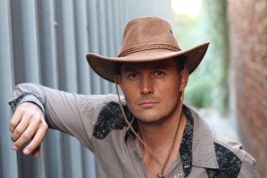 Duvara yaslanmış kovboy şapkalı yakışıklı genç adamın yakın plan portresi.