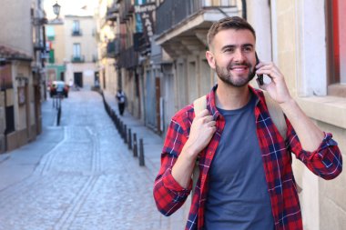 Sırt çantalı yakışıklı genç adamın eski şehir caddesinde telefonla konuşurken yakın plan portresi.
