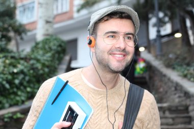 Yakından çekilmiş bir portre, günlük giysiler içindeki yakışıklı genç adam klasik kulaklıklarla müzik dinliyor ve şehir sokaklarında oyuncu.