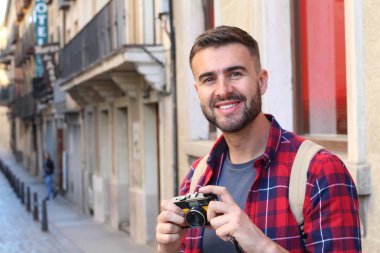 Eski şehir caddesinde sırt çantalı ve klasik kameralı yakışıklı bir gencin yakın plan portresi.