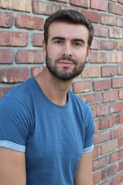 Tuğla duvarın önündeki mavi tişörtlü yakışıklı genç adamın yakın plan portresi.