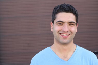 close-up portrait of handsome young man in blue t-shirt in front of brown wall