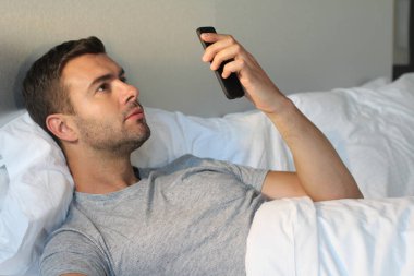 Evdeki yatakta akıllı telefon kullanan yakışıklı bir gencin yakın plan portresi.
