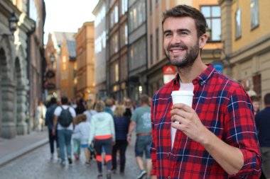 Sokakta elinde kağıt kahve olan yakışıklı bir gencin yakın plan portresi.