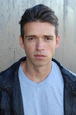 Gri duvarın önünde sıradan giyinmiş yakışıklı bir gencin yakın plan portresi.