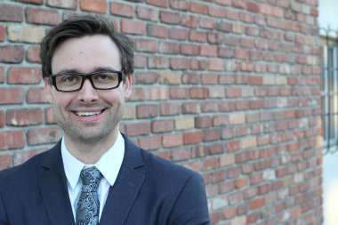 Tuğla duvarın önünde yakışıklı genç işadamının yakın plan çekimi.