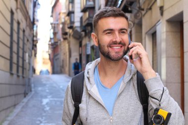 Eski şehir caddesinde telefonla konuşan yakışıklı bir gencin yakın plan portresi.