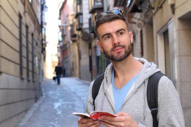 Sırt çantalı ve kitaplı yakışıklı genç adamın şehir sokaklarındaki yakın plan portresi.