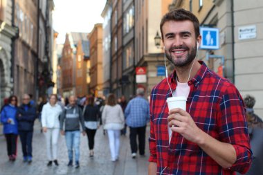 Sokakta elinde kağıt kahve olan yakışıklı bir gencin yakın plan portresi.