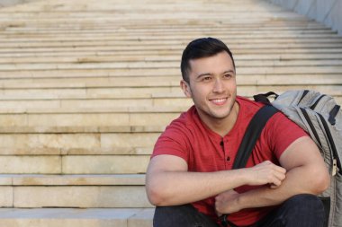 Yakından çekilmiş, sıradan giysiler içinde merdivenlerde oturan yakışıklı bir genç portresi.