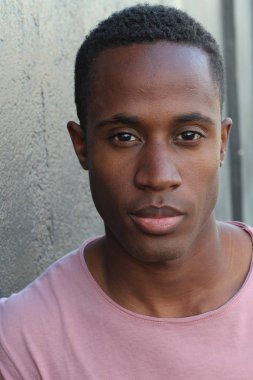 Gri duvarın önünde pembe tişörtlü yakışıklı genç adamın yakın plan portresi.