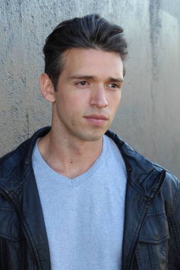 Gri duvarın önünde sıradan giyinmiş yakışıklı bir gencin yakın plan portresi.