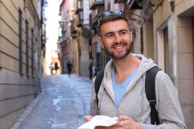 Sırt çantalı ve kitaplı yakışıklı genç adamın şehir sokaklarındaki yakın plan portresi.