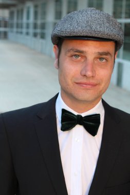 Siyah takım elbiseli, papyonlu ve şapkalı yakışıklı bir adamın yakın plan portresi.