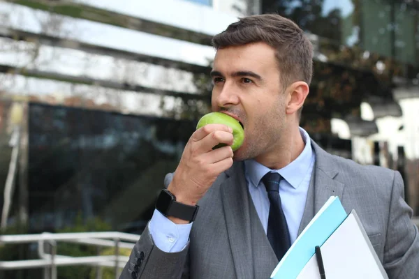 close-up portrait of handsome young businessman in suit eating green apple on street