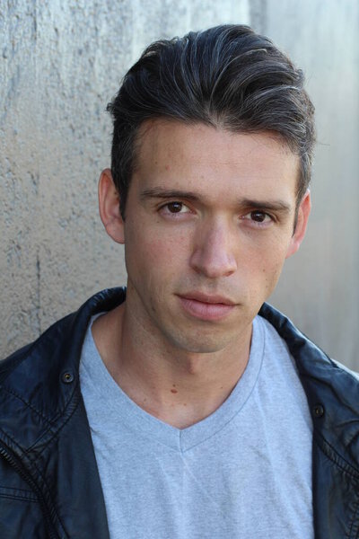 Крупный план портрета красивого молодого человека в повседневной одежде перед серой стеной
