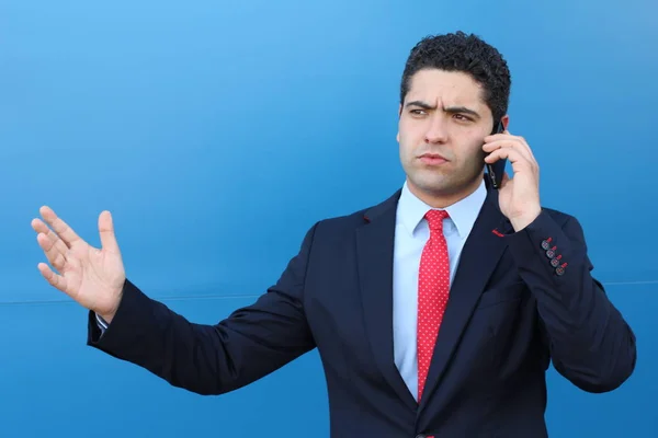 青い壁の前で電話で話しているハンサムな若いビジネスマンのクローズアップ肖像画 — ストック写真