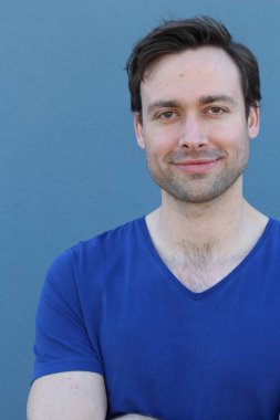 Mavi duvarın önünde sıradan giyinmiş yakışıklı bir gencin yakın plan portresi.