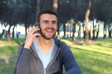 Yeşil Park 'ta telefonla konuşan sıradan giyinmiş yakışıklı genç adamın yakın plan portresi.